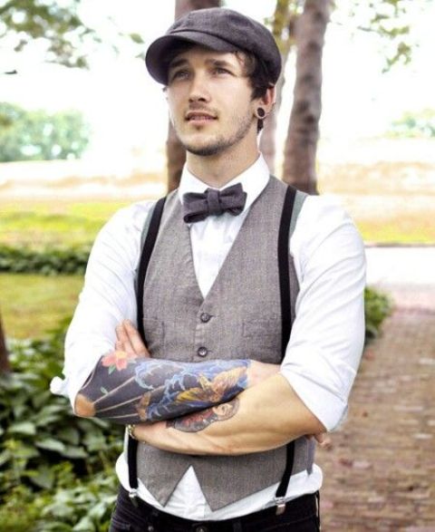 a vintage groom's look with a grey waistcoat, black pants and suspenders, a black bow tie and a black cap