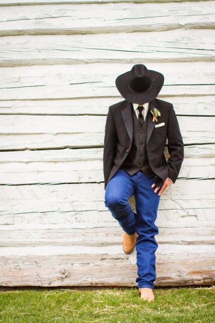 a rustic groom's look with jeans, a black waistcoat and jacket, a black hat and tie and a white shirt