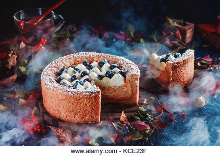 Cut cake with a shortbread crust on a dark background. A piece of cake with whipped cream and blueberries. Traditional - Stock Image