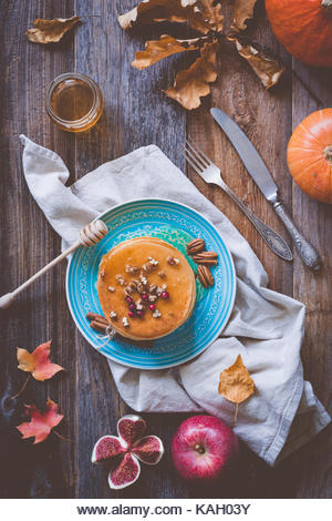 Pumkin pancakes on a blue plate on wooden background served with pecan nuts and honey. Autumn food still life - Stock Image