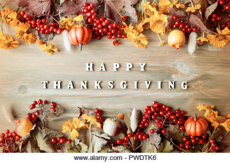 Thanksgiving day autumn background with Happy Thanksgiving letters, seasonal autumn nature berries, pumpkins, apples and flowers on the wooden backgro - Stock Image