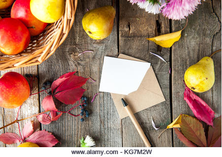 Thanksgiving background with seasonal fruits, flowers, greeting card and envelope on a rustic wooden table. Autumn - Stock Image