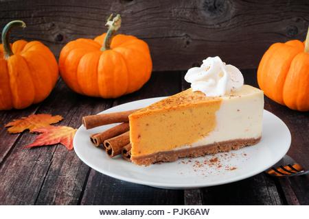 Slice of pumpkin cheesecake with whipped cream on a dark rustic wood background - Stock Image
