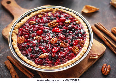 Autumn Pie on rustic background close up. Homemade seasonal pastry - berries and pecan pie or tart for Thanksgiving and autumn holidays. - Stock Image
