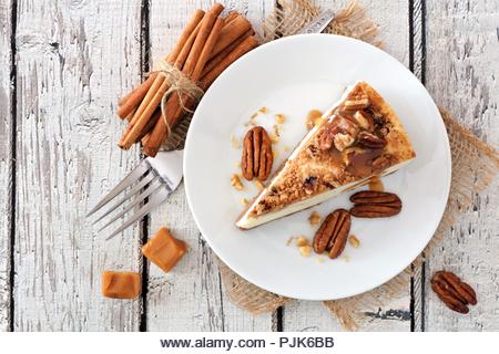 Slice of pecan caramel cheesecake, top view on a rustic white wood background - Stock Image