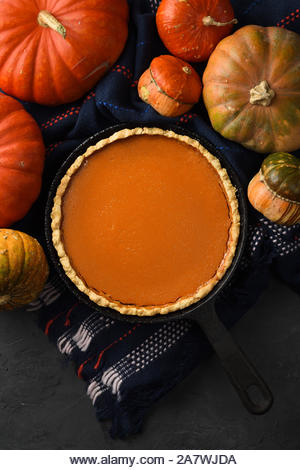 Hygge still life flat lay. Traditional pumpkin pie and winter squashes on black background copy space - Stock Image