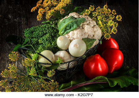 Mixed vegetables of cauliflower and broccoli, garlic, green onions, tomatoes and green peas on a wooden background in rustic style for Thanksgiving. - Stock Image