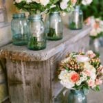 a wooden bench with lush floral centerpieces in pink and white and in blue jars
