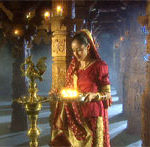 Hindu girl in temple holding lamp near gold statue