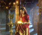 Hindu girl in temple holding lamp near gold statue
