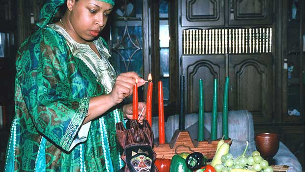 A woman in green African attire lights candles on a kinara