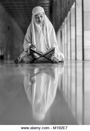 Islam girl reading Kuran inside Istiqlal Mosque during month of Ramadan, Jakarta, Indonesia - Stock Image