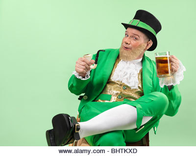Cheerful Leprechaun in bright green clothes holding a smoking pipe and a beer - Stock Image