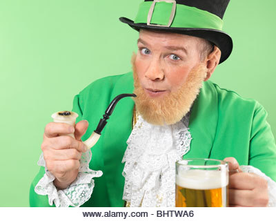 Cheerful Leprechaun in bright green clothes holding a smoking pipe and a beer - Stock Image