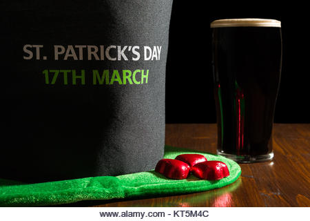 Closeup of St Patrick day with a pint of black beer and hat over a table - Stock Image