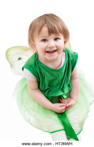 A pretty little girl with a cheeky smile wearing a green dress and fairy wings with shamrocks for Saint Patrick's - Stock Image