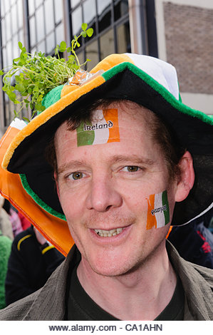 Belfast, UK. 17 Mar, 2012. Man with Irish Tricolour flag, green hat and shamrock watching the St Patrick Day parade - Stock Image
