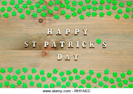 St Patrick's Day background. Green quatrefoils on the wooden background and wooden inscription Happy St Patrick's day, festive composition - Stock Image