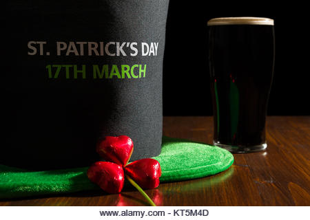 Closeup of St Patrick day with a pint of black beer, hat and shamrock over a table - Stock Image