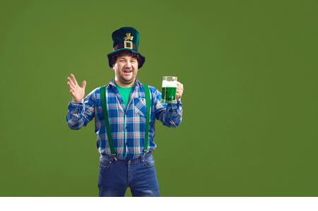 Happy guy celebrating Saint Patrick's Day and drinking beer isolated on green background - Stock Image