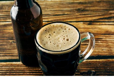 Close-up of the foam of a dark beer served in a mug on a wooden table. St. Patrick and stout concept - Stock Image