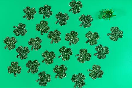 Flat lay composition with clover leaves and a green glass figurine on a green background. Saint Patrick day - Stock Image