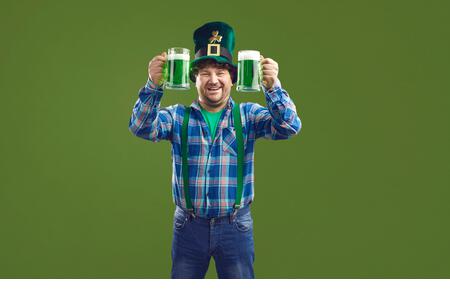 Happy man celebrating Saint Patrick's Day and drinking green beer from two glasses - Stock Image