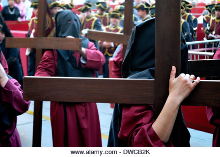 Penitents carrying large crosses in a Holy Week procession. - Stock Image