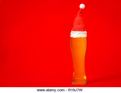 Full pilsner glass of pale lager beer or ale with Santa Claus or christmas red hat on red background - Stock Image