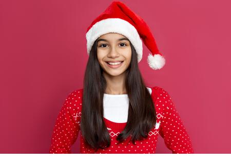 Smiling indian kid girl wear santa hat stand on red background, headshot portrait. - Stock Image