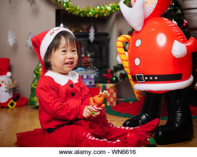 Cute Happy Girl In Santa Claus Costume Holding Toy - Stock Image