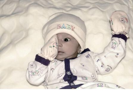 Closeup portrait image of cute beautiful adorable baby boy Asian Indian ethnicity in winter clothing lying of bed on white blanket. Sweet toddler posi - Stock Image