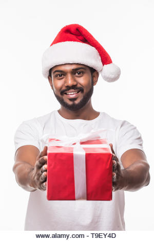 Happy indian man wearing santa hat and holding gift box isolated on white background - Stock Image