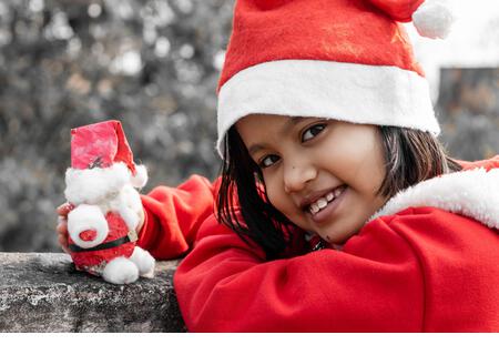 a cute Indian girl child playing with santa claus and looking at camera - Stock Image