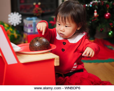 Close-up Of Cute Girl In Santa Claus Costume Touching Food - Stock Image