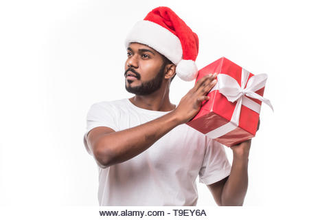 Happy indian man wearing santa hat and holding gift box isolated on white background - Stock Image