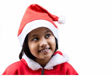 portrait of an Indian girl child smiling and looking aside in santa claus dress and hat - Stock Image