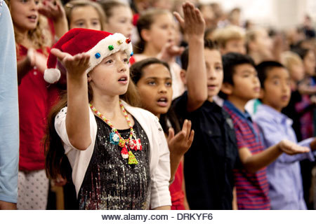 Multiracial middle school children sing Christmas carols as a group at a school concert in Aliso Viejo, CA. Note Santa Claus hat. - Stock Image