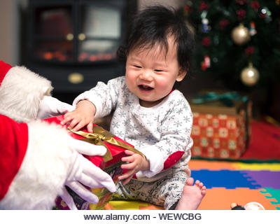 Cropped Hands Of Santa Claus Giving Gift To Baby Girl - Stock Image