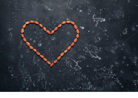 Heart shaped almonds on black stone grunge background. Valentine's Day. Top view - Stock Image