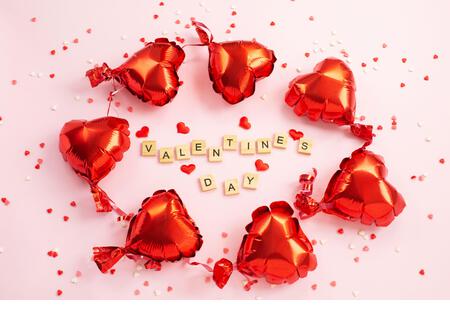 The word Valentine s Day from letter blocks and red hearts Foil balloons around. Romantic, St Valentines day concept. Top view. - Stock Image
