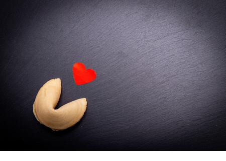 A fortune cookie with a little red heart on a black stone background. Are you ready to break the cookie and discover your love destiny? - Stock Image