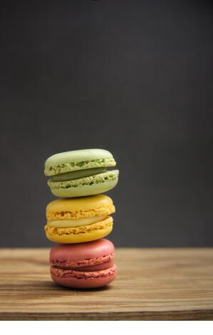A stack of macarons of different flavors and colors on a wooden table with dark background, side light and copy space - Stock Image