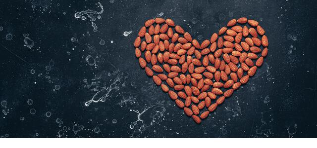 Heart shaped almonds on black stone grunge background, banner. Valentine's Day. Top view - Stock Image