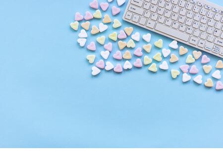 Heart shaped candies and keyboard computer on a blue table. Valentine's day concept. Top view, flat lay, copy space. - Stock Image