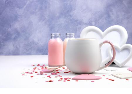 Round Cup with a drink on a romantic background with a frame and bottles of milk drink on a white and purple background. - Stock Image