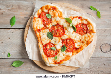 Heart shaped pizza Margherita over wooden background with copy space. Pizza with tomatoes, mozzarella cheese and - Stock Image