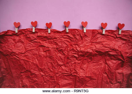 Clothespins with hearts hang on a rope on a colored background. Festive concept in minimal style for Valentine's Day or another love event. Below there is a place for text. - Stock Image