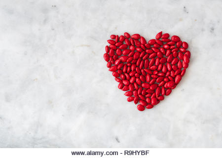 Red candy coated sunflower seeds in a heart shape on a white granite background for Valentine’s Day - Stock Image