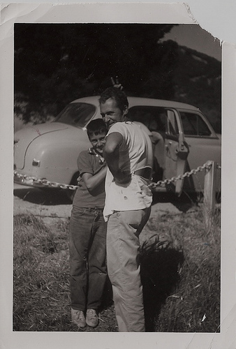 Vintage father and son standing in front of car.